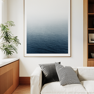 Modern living room with a white sofa, wooden bookshelf, and framed artwork of a blue ocean.