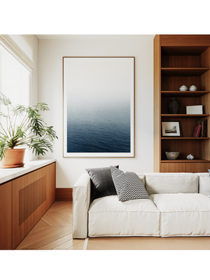 Modern living room with a white sofa, wooden bookshelf, and framed artwork of a blue ocean.