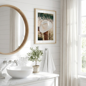 Bathroom with round mirror, sink, plant, and framed picture on white wall.