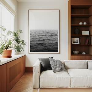 Modern living room with a white sofa, wooden bookshelf, and framed ocean picture.