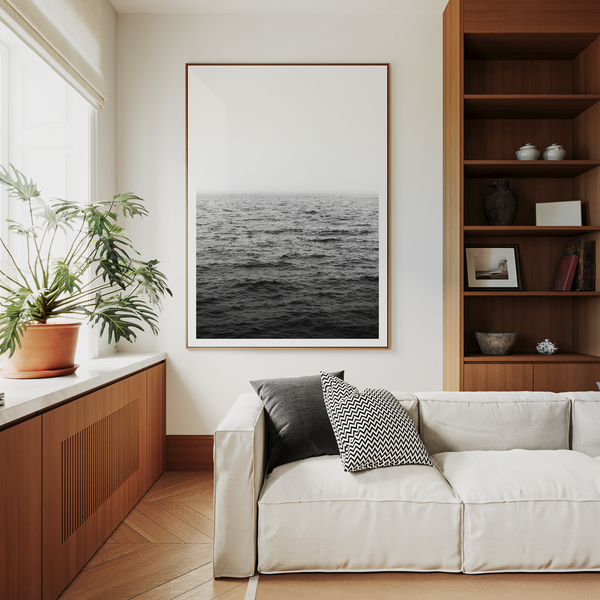 Modern living room with a white sofa, wooden bookshelf, and framed ocean picture.