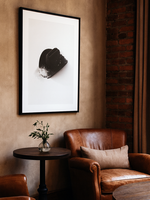 Cozy interior with a brown leather armchair, small round table, and framed artwork on a beige wall. Western Rustic Wall Art. 